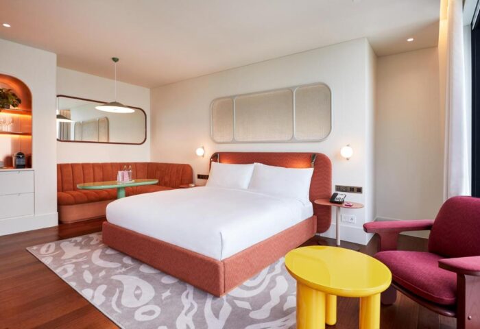 The Standard Bangkok Mahanakhon hotel room. Modern design, orange bed, sofa, and yellow table. Best gay hotel in Bangkok for LGBTQ+ travelers.