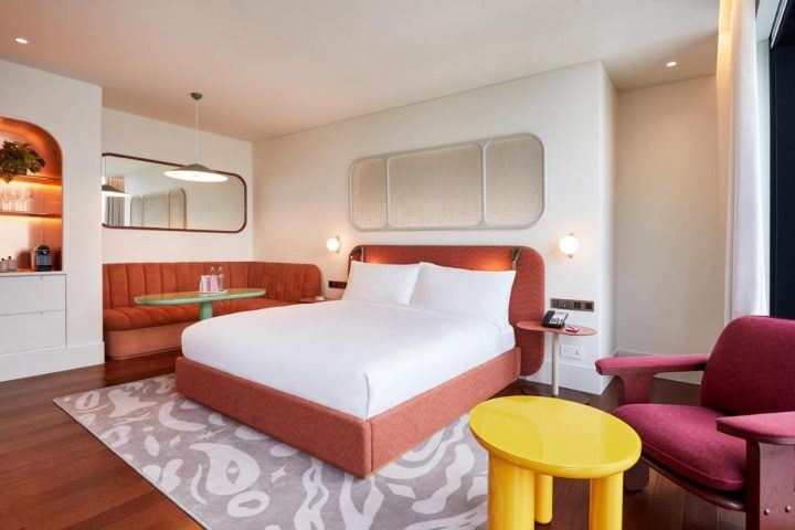 The Standard Bangkok Mahanakhon hotel room. Modern design, orange bed, sofa, and yellow table. Best gay hotel in Bangkok for LGBTQ+ travelers.