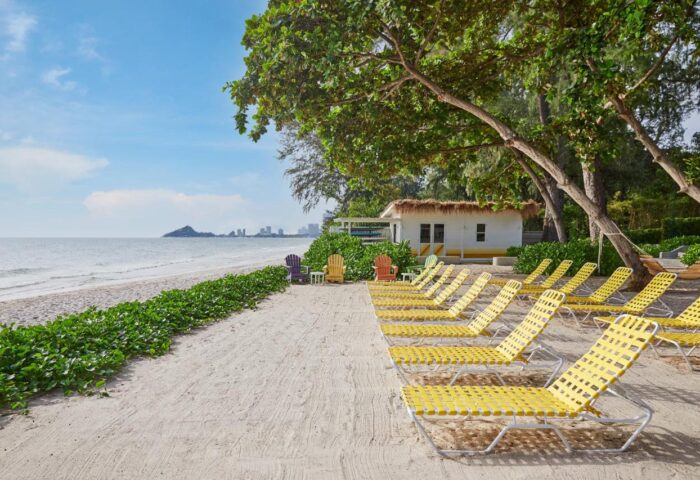 The Standard Hua Hin beach view with yellow loungers, white building, and sea. Ideal gay travel destination for relaxation.