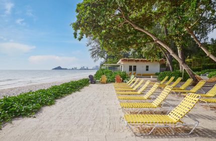 The Standard Hua Hin beach view with yellow loungers, white building, and sea. Ideal gay travel destination for relaxation.