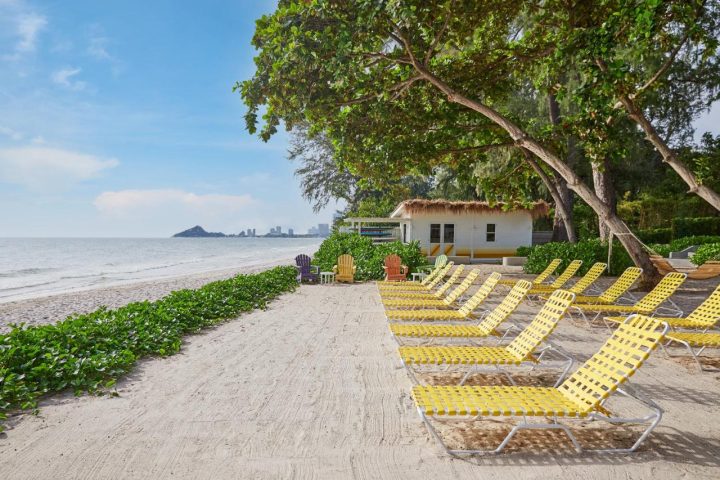 The Standard Hua Hin beach view with yellow loungers, white building, and sea. Ideal gay travel destination for relaxation.