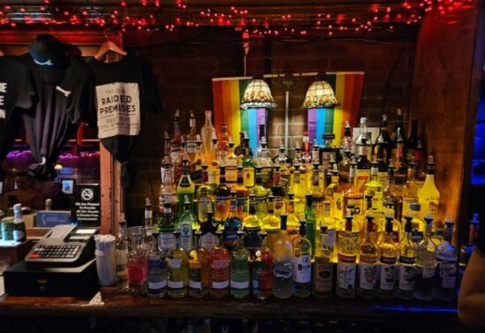 The Stonewall Inn bar in New York. Many liquor bottles, rainbow flag, and raided premises t-shirt. Gay travel destination.