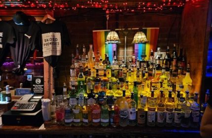 The Stonewall Inn bar in New York. Many liquor bottles, rainbow flag, and raided premises t-shirt. Gay travel destination.