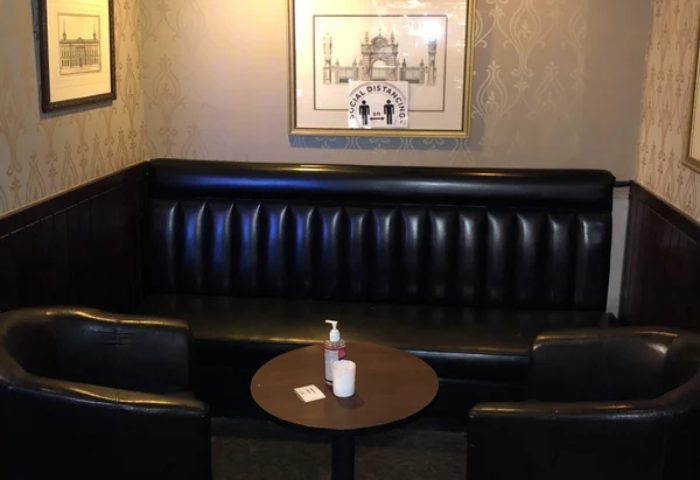 The Townhouse Bar in New York: A cozy booth with black leather seating, a small table, and social distancing signage. Gay travel advice.