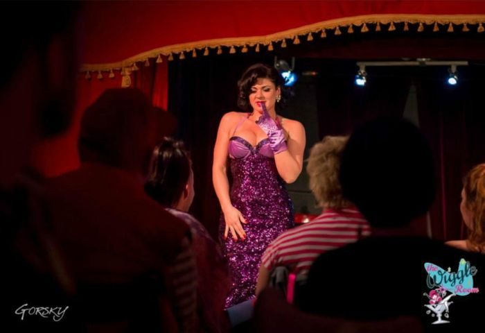 Drag queen performs at The Wiggle Room, a gay bar in Montreal. Live show with performer in purple sequin dress and gloves. Audience members watch.
