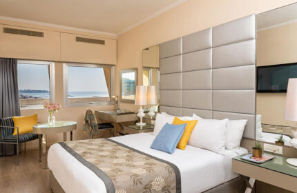Leonardo Art Tel Aviv By the Beach hotel room. Modern decor, sea view, desk, and bed with blue and yellow pillows. Honeymoon hotel idea.