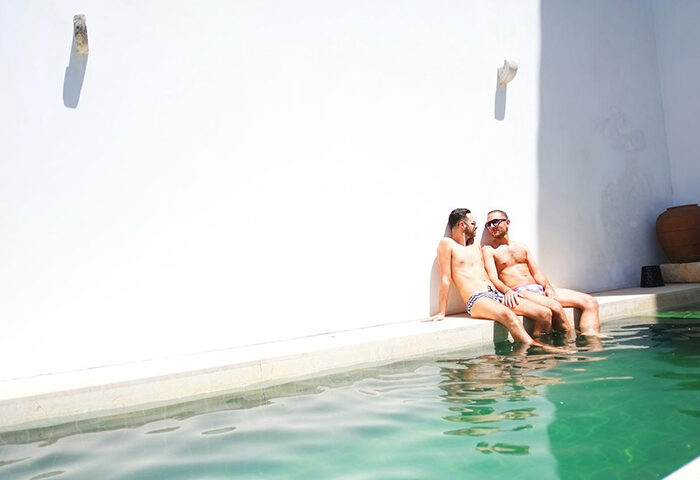 Gay men at The Late Birds Lisbon, a gay urban resort. Two men relax by the pool in swimsuits. Top-booked gay men-only hotel in Lisbon.