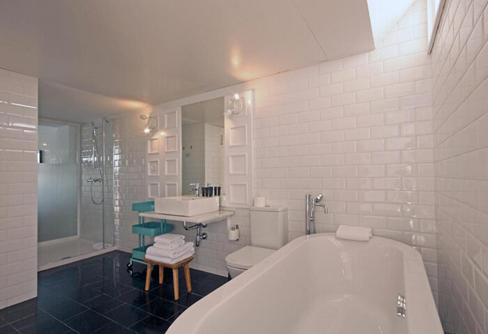 Bathroom at Gold Playa del Ingles, an adults-only gay hotel in Gran Canaria. Features a tub, shower, sink, and toilet with white subway tile.