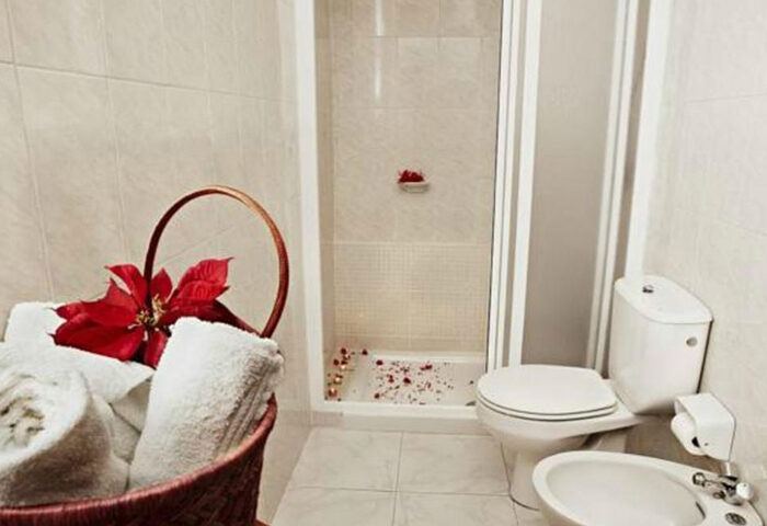 Gay Men Only Bungalows Tenesoya bathroom. Shower, toilet, bidet, and a basket with towels and a red flower. Budget hotel near Yumbo Center.