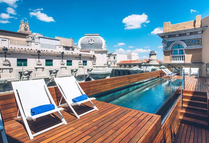 Iberostar Las Letras Gran Via rooftop pool in Madrid city center, perfect for gay honeymoon. Deck chairs, blue sky, and city views.