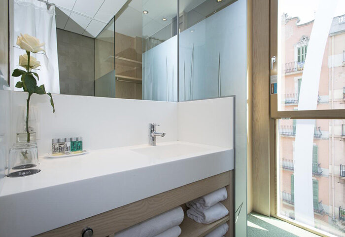 Ako Suites Hotel bathroom. Modern design with white countertop, sink, and towels. Window view. Best gay honeymoon hotel serviced apartment Barcelona.