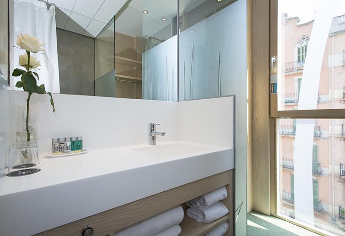 Ako Suites Hotel bathroom. Modern design with white countertop, sink, and towels. Window view. Best gay honeymoon hotel serviced apartment Barcelona.