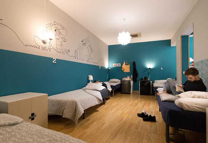 Sungate One, best gay hostel in Madrid's gayborhood for solo gay travelers. Dormitory with a man reading, blue walls, and cartoon art.