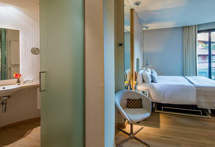Hotel Cram Barcelona room. Modern design, bathroom view, stylish chair, bed, and wooden floors. Best gay hotel option with pool.