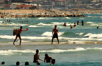 Tel Aviv Beach. People enjoy the water near Prima City Hotel. Gay travel to Israel. Men swimming, playing matkot. Sunny day, blue water.