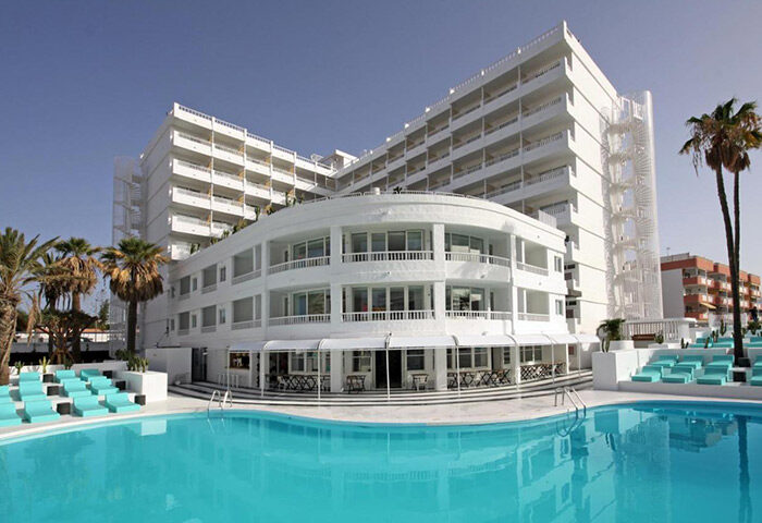 Gold Playa del Ingles Adults Only Hotel in Gran Canaria. Gay hotel with outdoor pool, white building, palm trees and blue sunbeds.