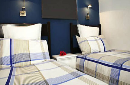 Bungalows Tenesoya, a gay men-only hotel in Playa del Ingles, Gran Canaria. Twin beds with plaid bedding in a modern room. Gay travel.