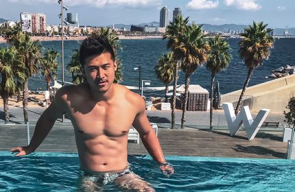 Gay man at W Barcelona, a luxury beachfront hotel. He's in the pool with the Barcelona skyline and palm trees in the background.