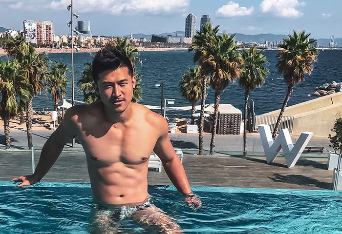 Gay man at W Barcelona, a luxury beachfront hotel. He's in the pool with the Barcelona skyline and palm trees in the background.