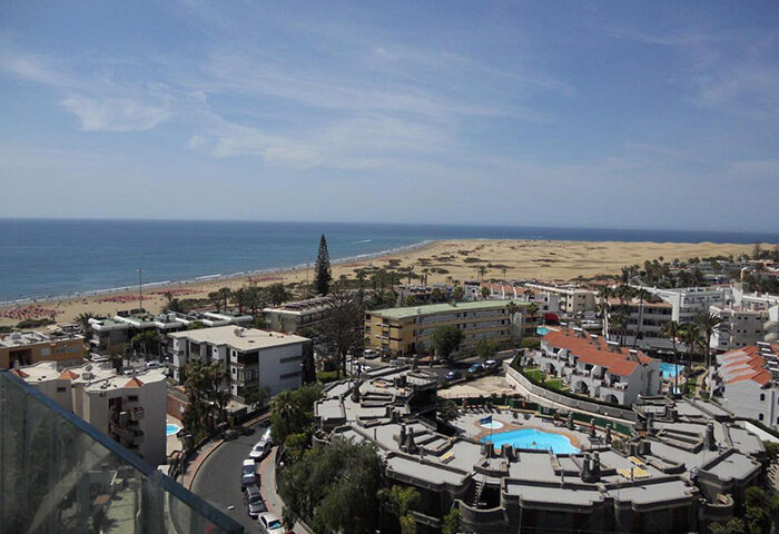 Aerial view of Playa del Ingles, Gran Canaria, from Bohemia Suites & Spa, an adults-only gay hotel. Beach, ocean, and dunes visible.