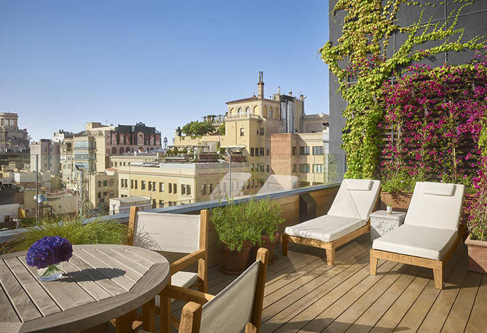Barcelona EDITION hotel rooftop terrace. Luxury gay hotel idea for wedding anniversary. Lounge chairs, table, flowers, city view.