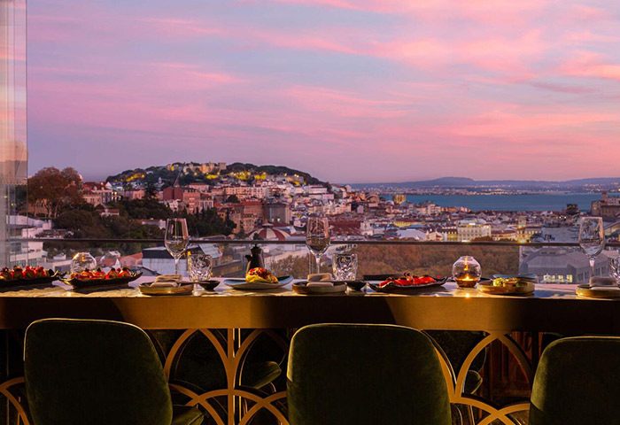 Tivoli Avenida Liberdade's sky bar in Lisbon, Portugal. Luxury gay hotel with city view, wine glasses, and plates of food at sunset.