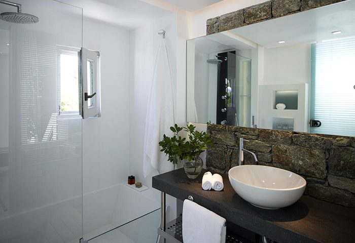 Semeli Hotel Mykonos bathroom. Luxury gay hotel in Mykonos Town, Chora city center. Stone detail, modern sink, shower, and window.
