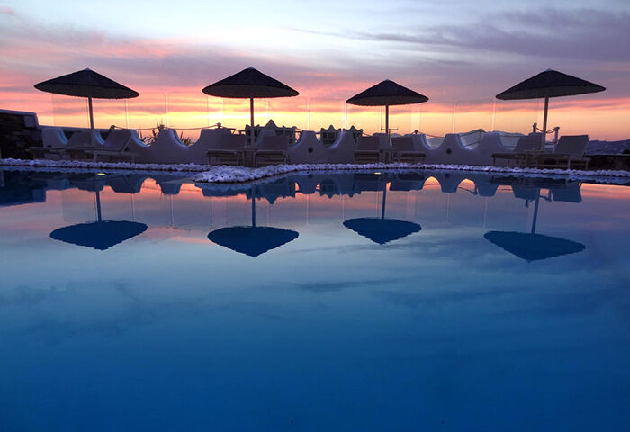 Ilio Maris, best gay hotel in Mykonos. Sunset view of pool with umbrellas reflecting in the water. Gayborhood upscale hotel.