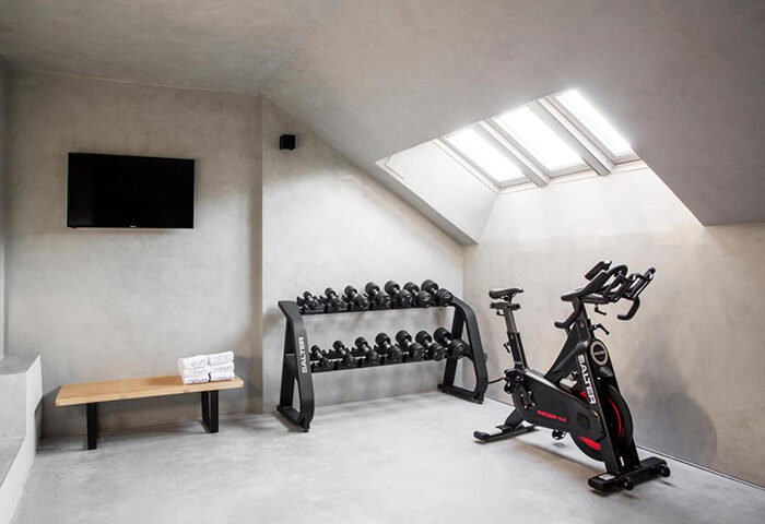 Urban Hotel Madrid city center gym. A wellness area with weights, exercise bike, TV, bench, and skylight. Luxury gay hotel for gay men travel.