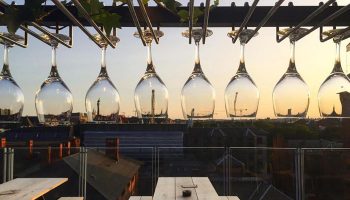 Hotel Danmark rooftop bar in Copenhagen's gayborhood. Wine glasses hang above tables, city skyline visible. A gay hotel in Vesterbro.