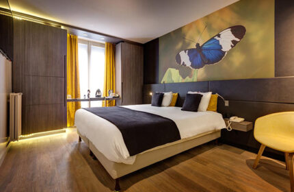 Hotel Elixir, a gay hotel in Paris' Marais gayborhood. Modern room with butterfly art, bed, desk, & yellow accents. Gay travel lodging.