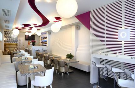 Matogianni Hotel's gay-friendly bar in Mykonos Town. Stylish interior with white seating, modern lighting, and a vibrant, welcoming atmosphere.