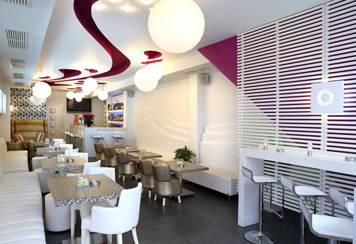 Matogianni Hotel's gay-friendly bar in Mykonos Town. Stylish interior with white seating, modern lighting, and a vibrant, welcoming atmosphere.