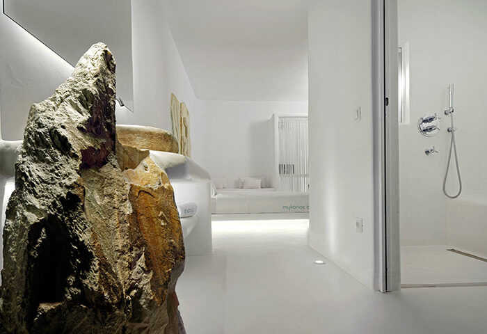 Mykonos Bay Resort room with stone decor, shower, and bed. Honeymoon beachfront hotel idea in Mykonos Town for gay couples.