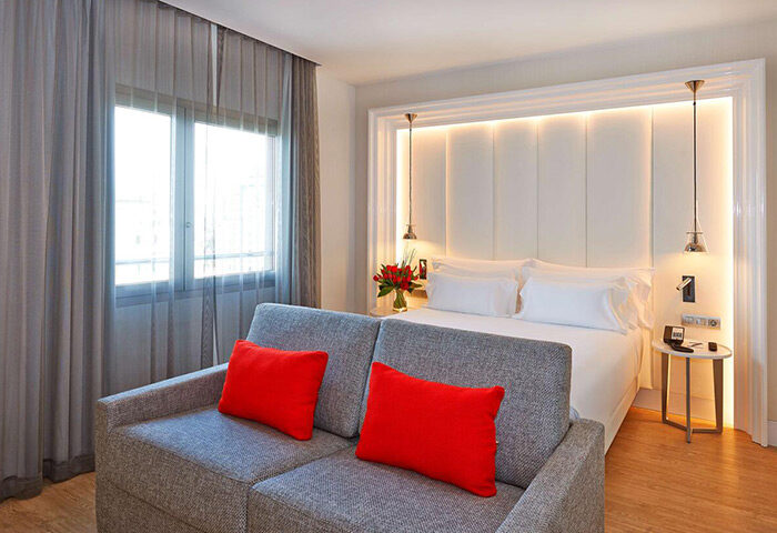 NH Collection Barcelona Gran Hotel Calderon room. Gay-friendly hotel in Eixample Gayborhood. Modern interior, bed, sofa, red pillows.