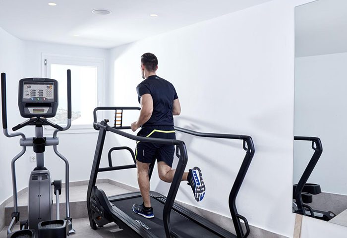 Absolute Mykonos Suites gym. Man runs on a treadmill. Most booked gay hotel in Mykonos Town. Fitness center at gay-friendly hotel.