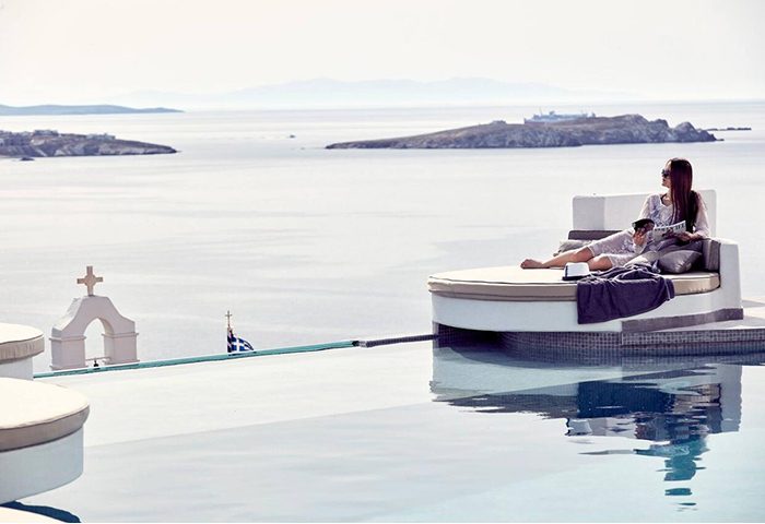 Absolute Mykonos Suites: Woman relaxes by infinity pool overlooking Mykonos Town. Popular gay hotel for travel advice and luxury vacations.