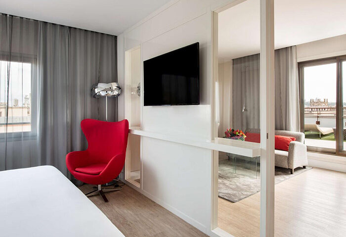 NH Collection Barcelona Gran Hotel Calderon suite. Modern design, red chair, TV, and balcony. Luxury gay hotel, Barcelona.