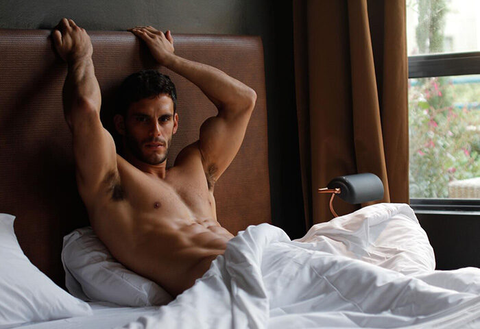 Shirtless man in bed at Inta Hotel, a popular gay adult-only hotel in Tel Aviv Jaffa. Best hotel for gay men's travel in Tel Aviv.
