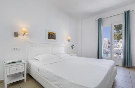 Carbonaki Hotel, Mykonos: White bedroom. A popular gay honeymoon hotel with a double bed, balcony view and bedside table.