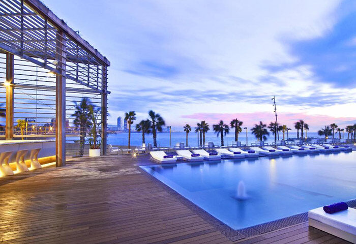 W Barcelona gay hotel infinity rooftop pool. View of the pool, palm trees, and beach. One of Barcelona's best gay hotels for gay men travelers.