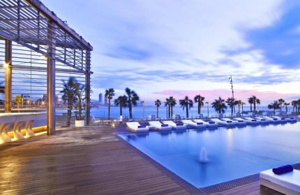 W Barcelona gay hotel infinity rooftop pool. View of the pool, palm trees, and beach. One of Barcelona's best gay hotels for gay men travelers.