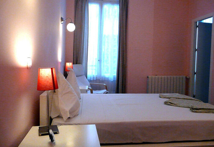 Hostal Pizarro room in Madrid city center, Chueca gayborhood. Pink walls, white bed, bedside lamps, window with curtains. Gay hostel.
