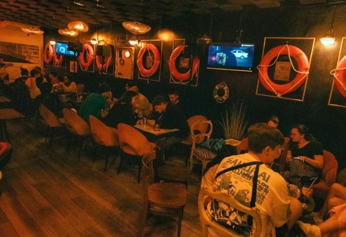 Interior of Titanic Bar, a gay bar in Barcelona. People sit at tables under life preserver decorations. Gay travel advice.