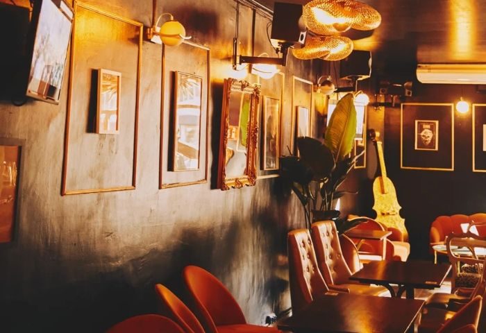 Interior of Titanic Bar, a gay bar in Barcelona. Warm lighting, orange chairs, mirrors, & a cello create a cozy, vintage atmosphere.