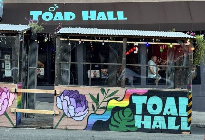 Toad Hall Bar in San Francisco. Gay bar exterior with rainbow art, flowers, and a man inside. Gay travel destination in San Francisco.