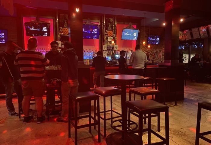 Interior of Toad Hall Bar in San Francisco, a gay bar. People at bar, stools, tables, TVs, and red lighting. Gay travel advice.