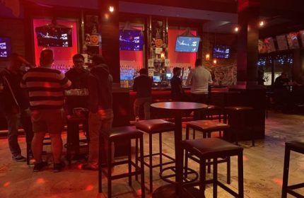 Interior of Toad Hall Bar in San Francisco, a gay bar. People at bar, stools, tables, TVs, and red lighting. Gay travel advice.
