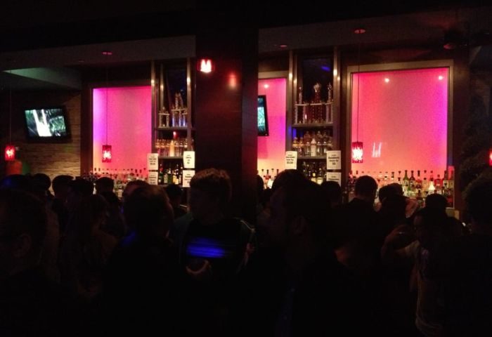 Interior of Toad Hall Bar in San Francisco. Gay bar with pink lighting, liquor bottles, and patrons. Gay travel advice for a fun night out.