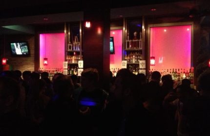 Interior of Toad Hall Bar in San Francisco. Gay bar with pink lighting, liquor bottles, and patrons. Gay travel advice for a fun night out.